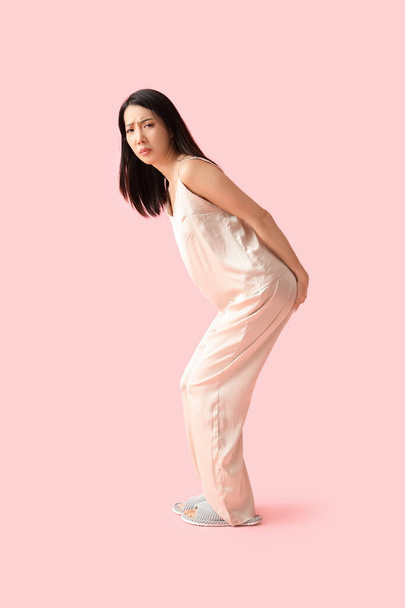 ピンクの背景に痔を持つパジャマの若いアジアの女性 - 写真・画像