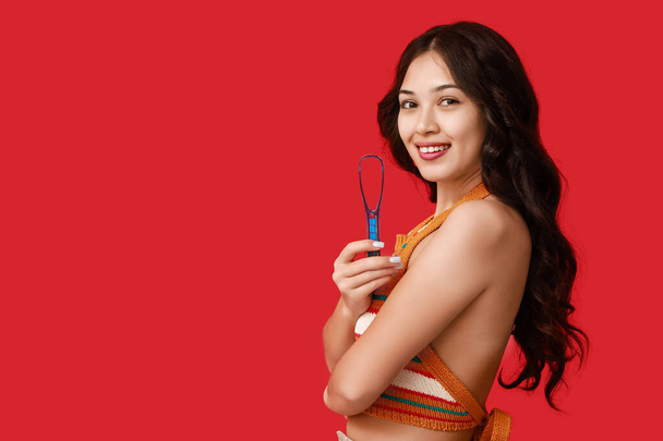 Onnellinen nuori aasialainen nainen kielen kaavin punaisella taustalla - Valokuva, kuva