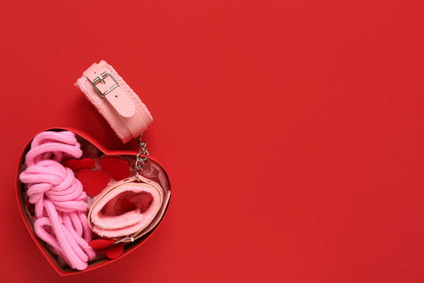 Gift box with rope and handcuffs from sex shop on red background - Photo, Image