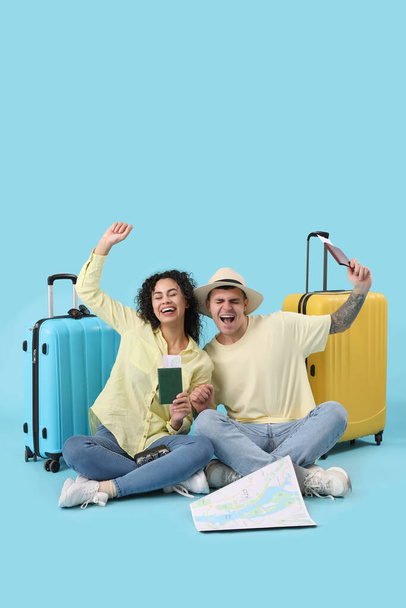 Χαρούμενο ζευγάρι τουριστών με βαλίτσες, διαβατήρια και χάρτη σε μπλε φόντο - Φωτογραφία, εικόνα