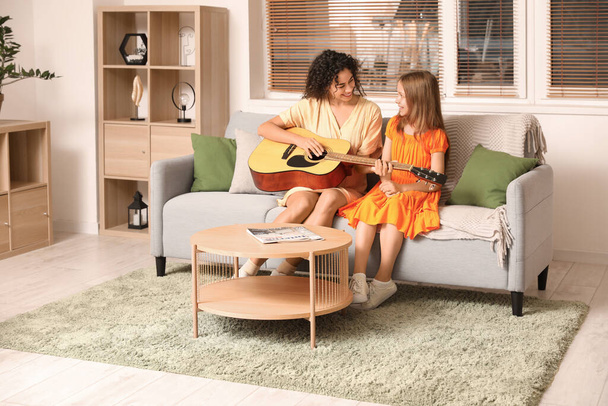 Νεαρή γυναίκα δίνει μαθήματα μουσικής σε έφηβη κοπέλα με ακουστική κιθάρα στο σπίτι - Φωτογραφία, εικόνα