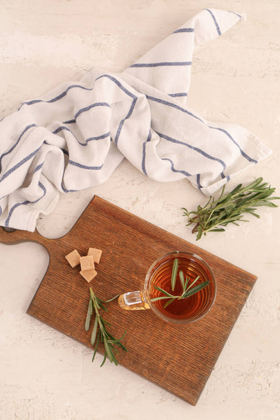 Wooden board with glass cup of hot rosemary tea and sugar on white background - Photo, Image