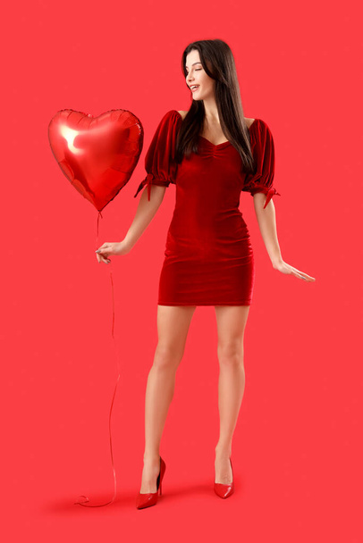 Beautiful young woman with heart-shaped air balloon on red background. Valentine's day celebration - Photo, Image