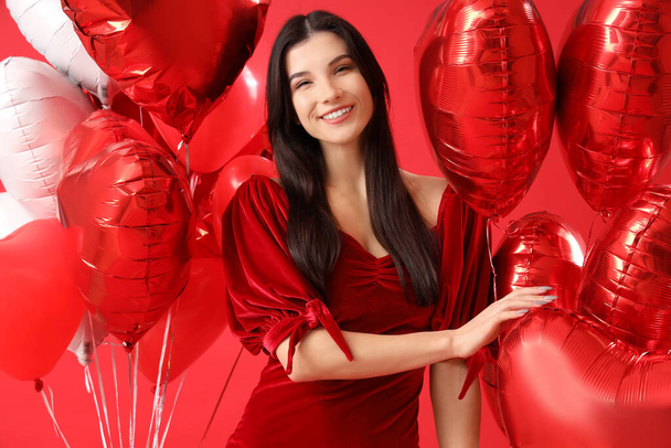 Kırmızı arka planda kalp şeklinde balonları olan güzel genç bir kadın. Sevgililer Günü kutlaması - Fotoğraf, Görsel