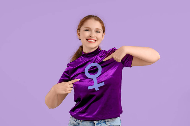 Young woman pointing at gender symbol on lilac background - Photo, Image