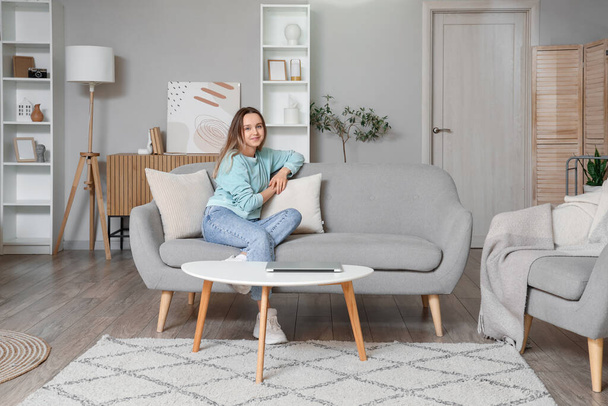 Mladá žena sedí na šedém gauči v obývacím pokoji - Fotografie, Obrázek