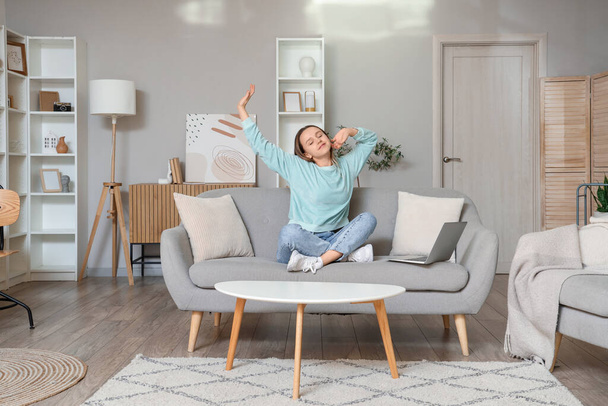 Young woman stretching on grey couch in living room - Foto, Imagen