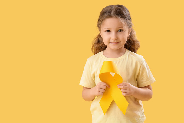 Schattig klein meisje met geel lint op kleur achtergrond. Bewustmakingsconcept voor kinderkanker - Foto, afbeelding