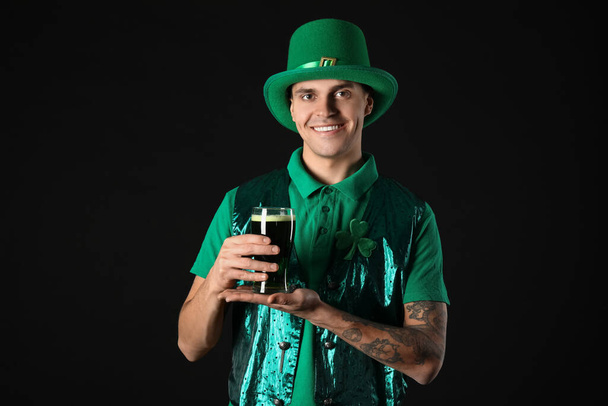 Boldog fiatalember zöld ruhában és sörrel a sötét háttérben. Szent Patrik nap - Fotó, kép