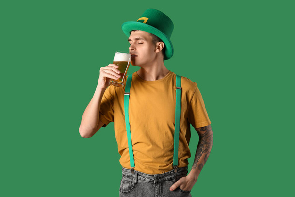 Jovem de chapéu de duende a beber cerveja no fundo verde. Dia de São Patrício - Foto, Imagem