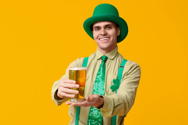 Щасливий молодий чоловік в капелюсі лепречуна і зі склянкою пива на жовтому тлі. День святого Патріка - Фото, зображення