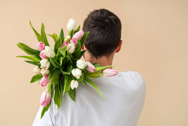 Młody człowiek z bukietem pięknych tulipanów na beżowym tle. Międzynarodowy Dzień Kobiet - Zdjęcie, obraz