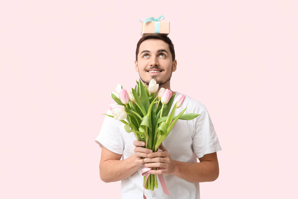 Fiatal férfi csokor gyönyörű tulipánokkal és ajándékdobozzal rózsaszín háttérrel. Nemzetközi nőnap - Fotó, kép