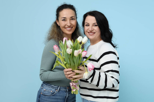 Happy mature women with bouquet of beautiful tulips on blue background. International Women's Day - Photo, Image