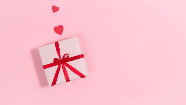 Red hearts, symbols of love near gift box tied with a red ribbon. Greeting card. Valentine's day holiday. Pink background. Copy space. Flat lay. - Fotoğraf, Görsel