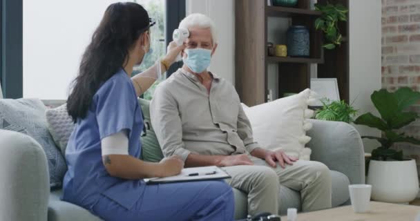 Thermometer, clipboard and caregiver check old man for fever virus, cold disease and health problem in retirement home. Mask, patient assessment and nurse writing test results of temperature reading. - Footage, Video