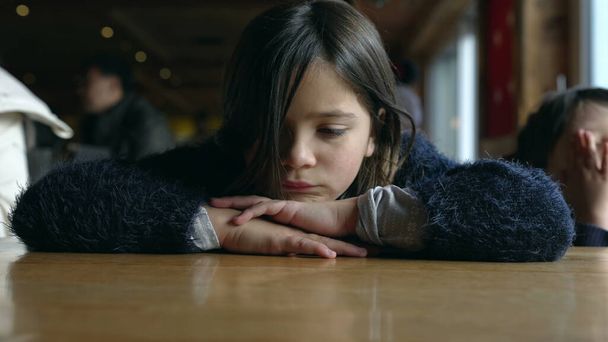 Depressives Kind mit dem Kopf auf dem Tisch, das tiefe Traurigkeit empfindet. Melancholisches 8-jähriges Kind mit gesenktem Kopf auf Tisch - Foto, Bild