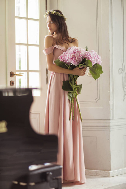 Piękna kobieta w długiej sukience z bukietem kwiatów we wnętrzu pałacu. - Zdjęcie, obraz