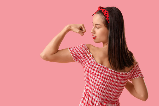 Retrato de una fuerte mujer pin-up mostrando músculos sobre fondo rosa. Mes de Historia de la Mujer - Foto, imagen