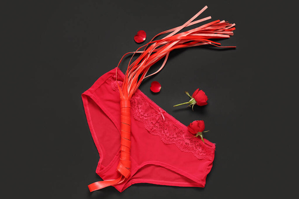 Composition with female panties, whip from sex shop and rose flowers on dark background. Valentine's Day celebration - Photo, Image