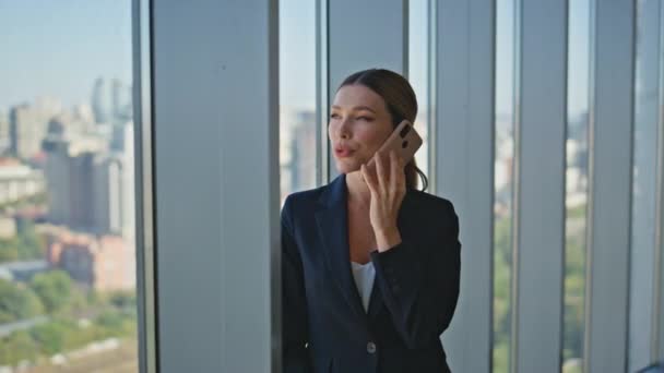 Kadın patron panoramik pencerede hücreden konuşuyor. Şehir manzarasında şirket profesyoneli iş görüşmeleri yapıyor. Güzel bir ofis çalışanı cep telefonuyla iletişim kuruyor. Emlakçı - Video, Çekim
