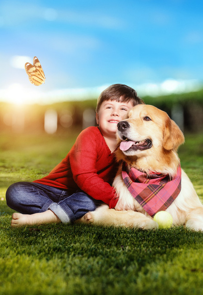 Kleine jongen met een gouden retriever hond zittend op het gras - Foto, afbeelding