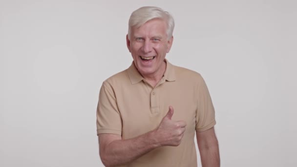 El hombre de pelo gris positivo sonríe a la cámara. mostrando el signo de pulgar hacia arriba sobre un fondo blanco. Imágenes de alta calidad 4k - Imágenes, Vídeo