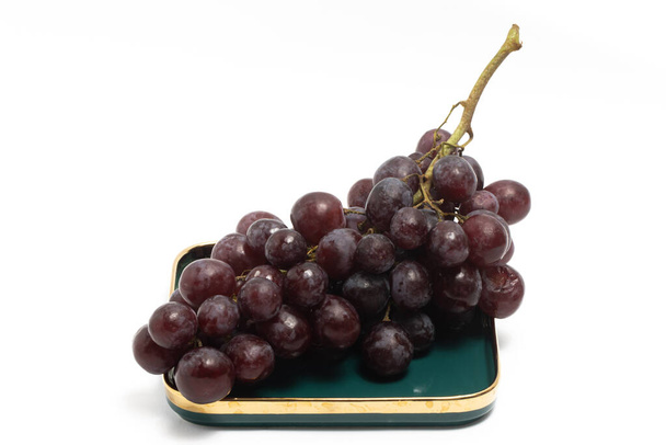 Un ramo de uvas rojas orgánicas frescas deliciosa fruta en un plato verde aislado en el camino de recorte de fondo blanco - Foto, imagen