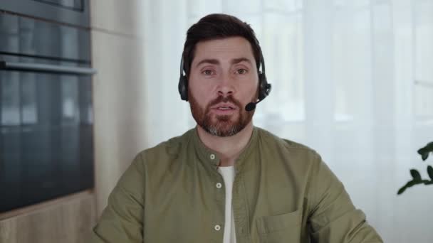 Első személy nézete magabiztos távoli munkavállaló visel vezeték nélküli headset beszél videokonferencia során otthon. Kaukázusi férfi alkalmi khaki ingben ül az asztalnál és online találkozót tart. - Felvétel, videó