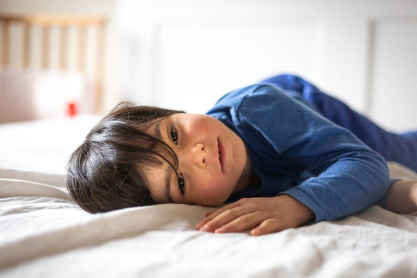 青い服を着たベッドの子供に横たわるクローズアップ肖像画 - 写真・画像
