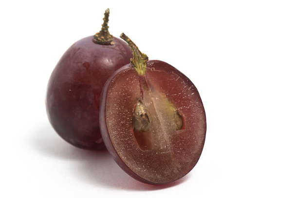 Primer plano en rodajas de uvas rojas orgánicas frescas deliciosa fruta con una rama aislada en el camino de recorte de fondo blanco - Foto, imagen