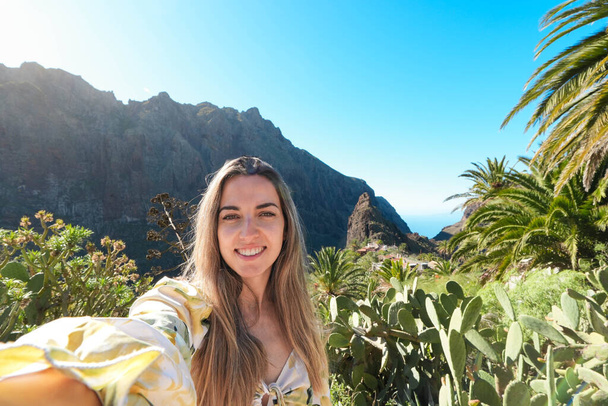 Egy nő megragad egy emlékezetes pillanatot, amikor szelfit készít egy lenyűgöző hegyi táj előtt Masca Valley-ben, Tenerife-ban.. - Fotó, kép