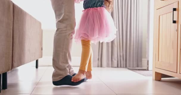Father, child and dancing on feet in living room, modern home and music or radio with love. Learning, energy and girl in ballerina dress by man bonding and standing by daughter in apartment with care. - Footage, Video