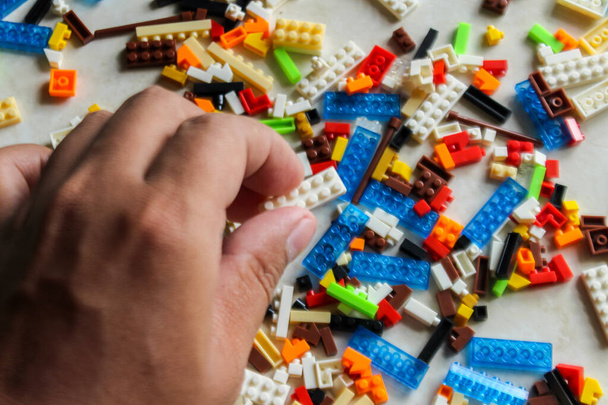 Bovenhoek uitzicht van de hand houden lego bakstenen op witte achtergrond. man hand rangschikken stapel van kleurrijke Lego blokken. - Foto, afbeelding