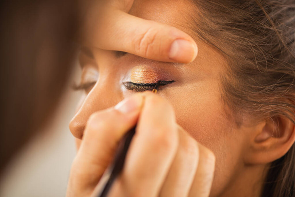 Κοντινό πλάνο ενός make-up καλλιτέχνη να πάρει eyeliner σε ένα χαριτωμένο νεαρό μοντέλο. - Φωτογραφία, εικόνα