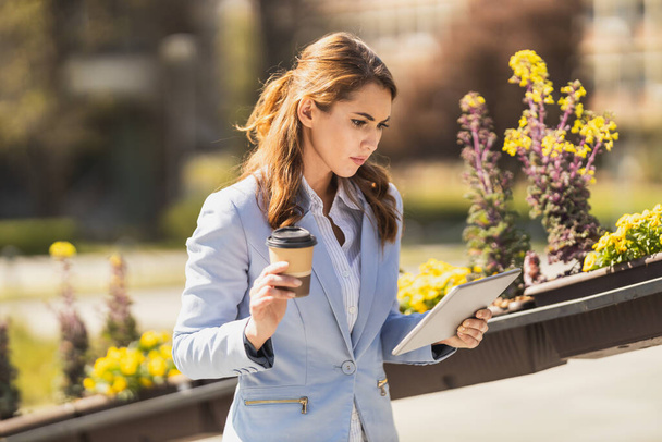 Молода стурбована бізнес-леді з планшетом в руках стоїть перед офісом під час перерви на каву. - Фото, зображення