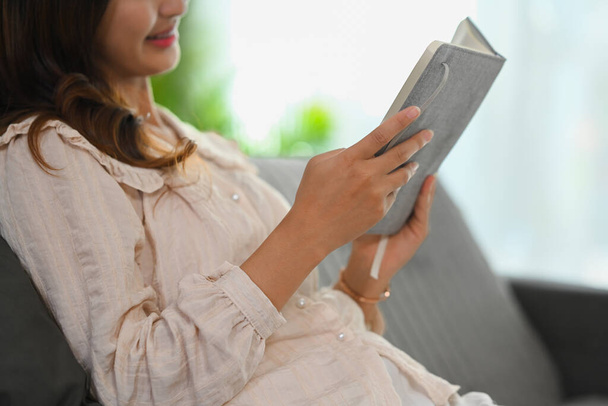 Gehakt schot gelukkige jonge vrouw in casual kleding lezen boek op de bank thuis. - Foto, afbeelding