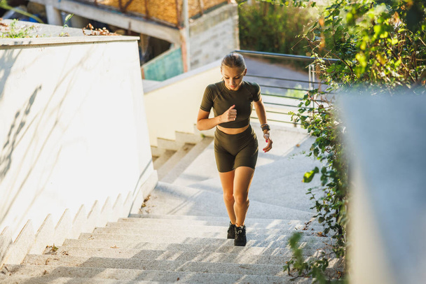 A sporty young woman walking up the stairs while warming up before outdoor working out. - Photo, Image