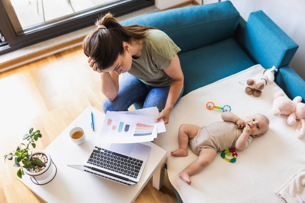 Tourné d'une jeune mère occupée regardant stressé tout en travaillant à la maison tout en prenant soin de son adorable bébé. - Photo, image
