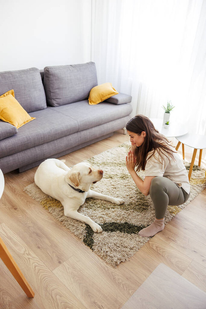 Active young woman in sportswear doing yoga at home with her pet dog by her side - Photo, Image