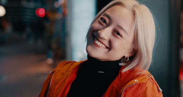 Woman, portrait and smile in city at night on Japanese street for explore, vacation or bokeh. Female person, face and happy in urban town for party adventure for tourism travel, fashion or confidence. - Photo, Image