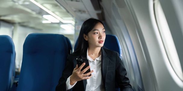 Hermosa mujer de negocios asiática utilizando el teléfono móvil en avión. trabajo, viajes, concepto de negocio. - Foto, imagen