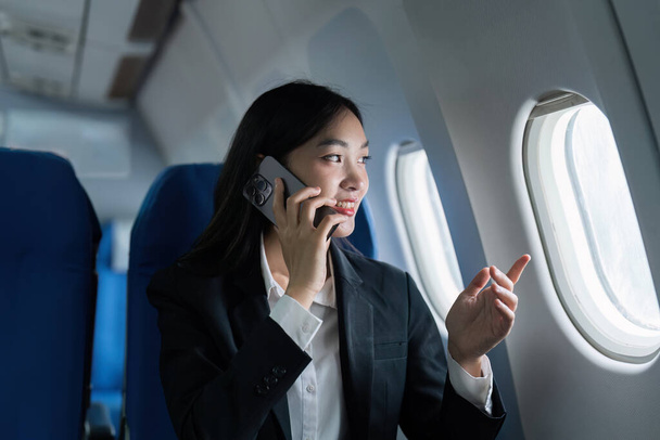 Hermosa mujer de negocios asiática hablando con teléfono móvil en avión. trabajo, viajes, concepto de negocio. - Foto, imagen