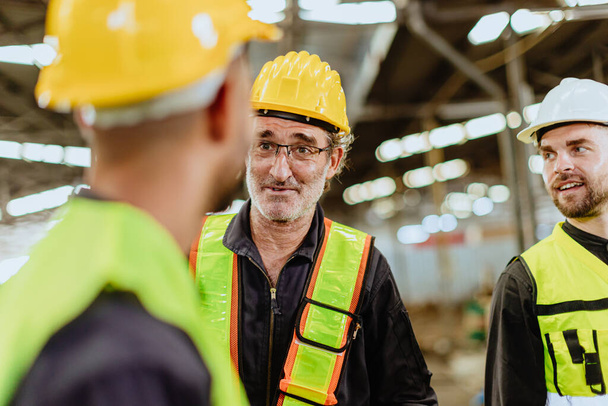 vanhempi ammatillinen insinööri miespuolinen työntekijä onnellinen puhuminen nuoren miehen tehtaan työntekijöiden kanssa teollisuudessa työpaikalla. - Valokuva, kuva