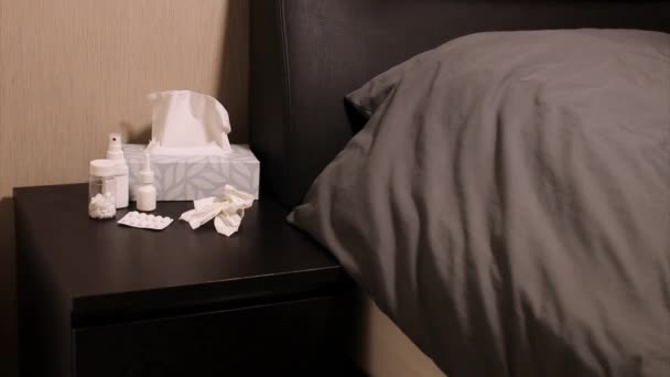 Pillen, neusspray, keelspray en een thermometer op een nachtkastje bij bed, ziek thuis concept - Video