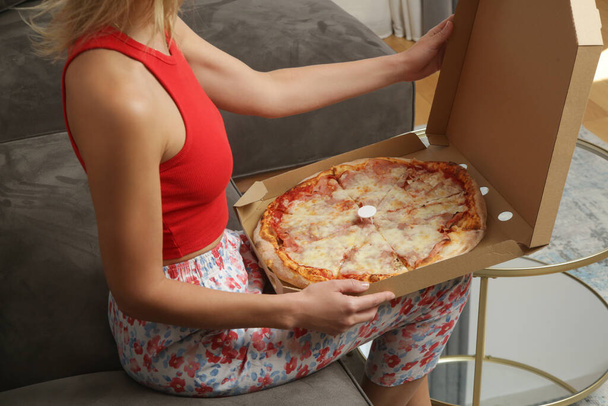 Nő eszik elvitelre pizza dobozból, miközben otthon pihen a kanapén - Fotó, kép