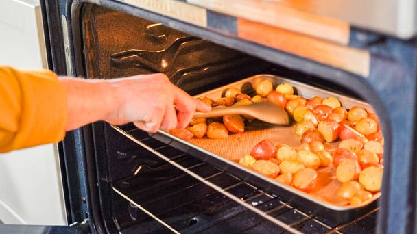 В обстановке современной кухни молодой человек погружается в приготовление ужина, в настоящее время обжаривая в духовке приправленный радужный картофель, важный шаг к восхитительной трапезе.. - Фото, изображение