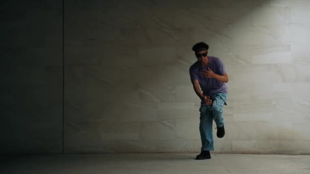 Zkušený chytrý pouliční tanečník cvičit b-boy pohyb v budově s šedým pozadím. Mladý pohledný choreograf provádí energický a aktivní pohyb. Venkovní sport2024. Vesele. - Záběry, video