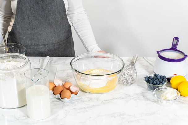 Zutaten in einer Glasschüssel kombinieren, gekonnt mit einem Schneebesen rühren, um einen köstlichen Vanillekuchen zuzubereiten. - Foto, Bild