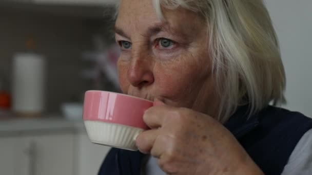Близько кавказької 60-х років жінка сидить біля вікна п'є каву латте або чай на кухні. Красива жінка насолоджується випивкою кави в кафе.  - Кадри, відео
